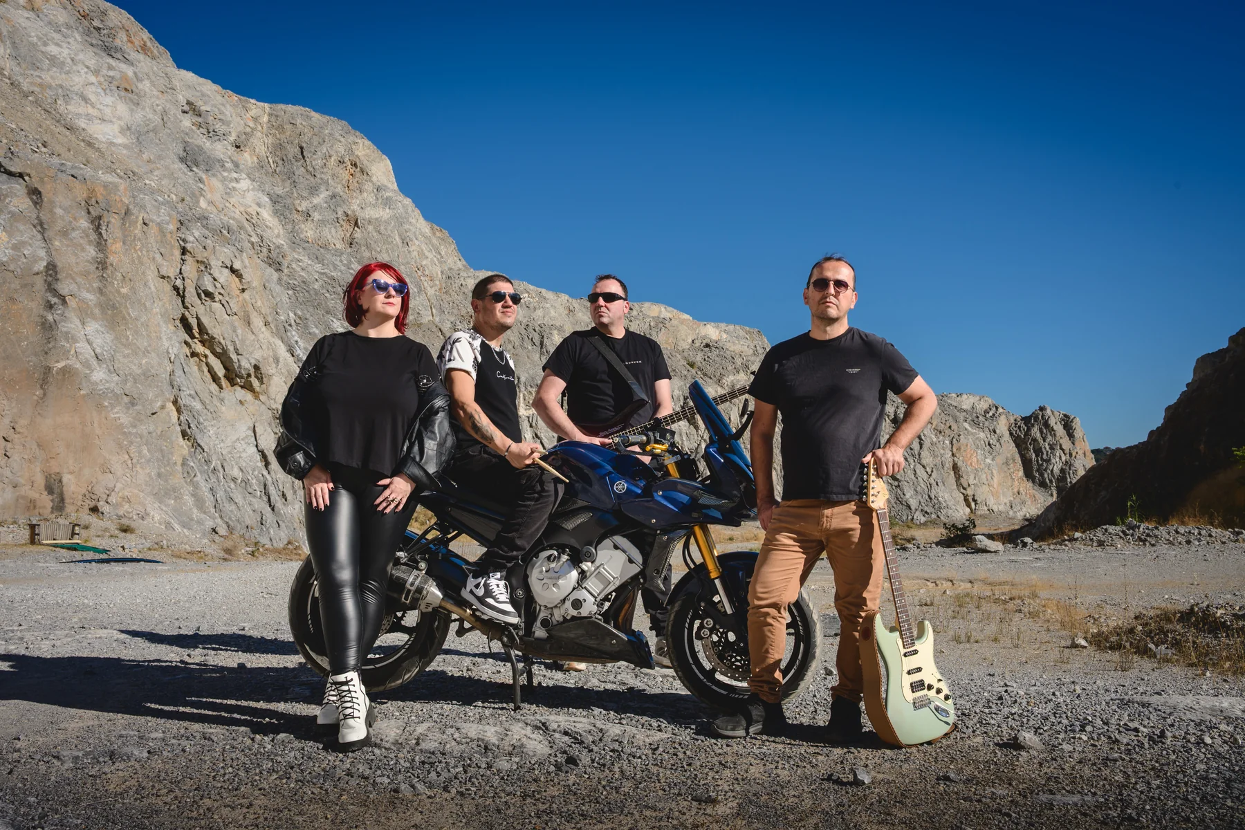 Rust n Groove with their instruments and a motorcycle at the quarry, under a deep blue sky.